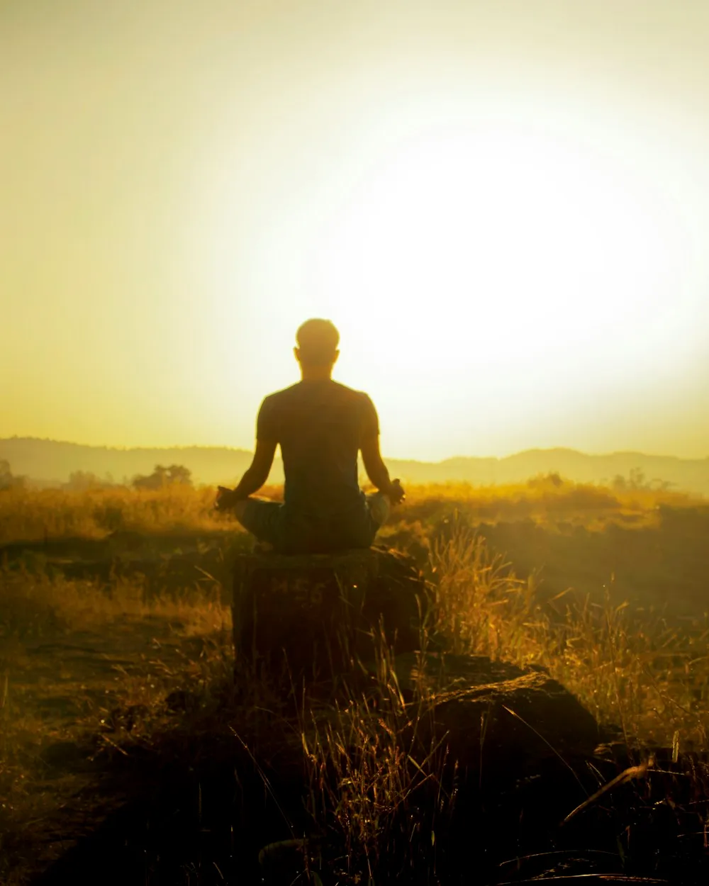 A person meditating at sunrise on a hillside